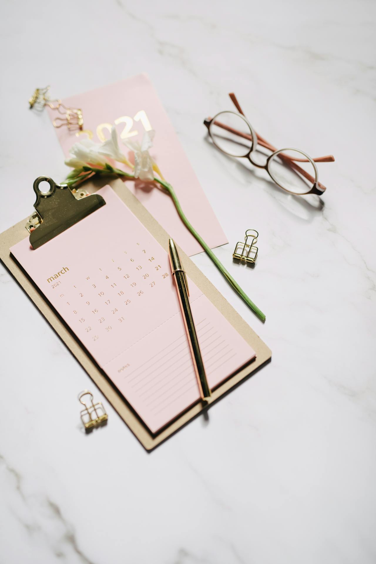 Black Framed Eyeglasses Near a Flower and a Clipboard on Paper